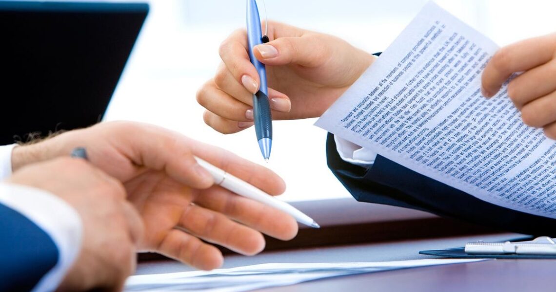 Deux mains échangent un stylo et des papiers sur un bureau