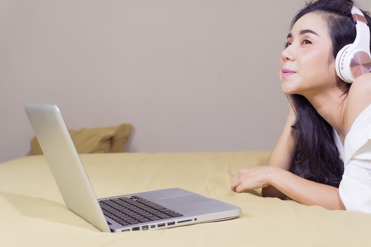 Une femme au lit écoute de la musique via casque sur ordinateur portable